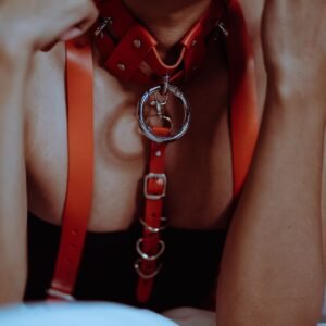 Crop anonymous sensual female in provocative BDSM collar biting leather belt while lying on bed